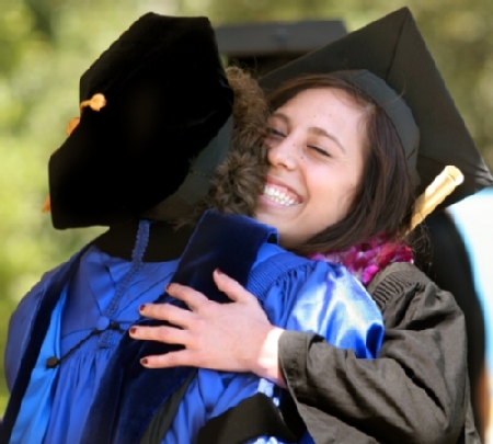 two graduates in cap and gown happily hugging